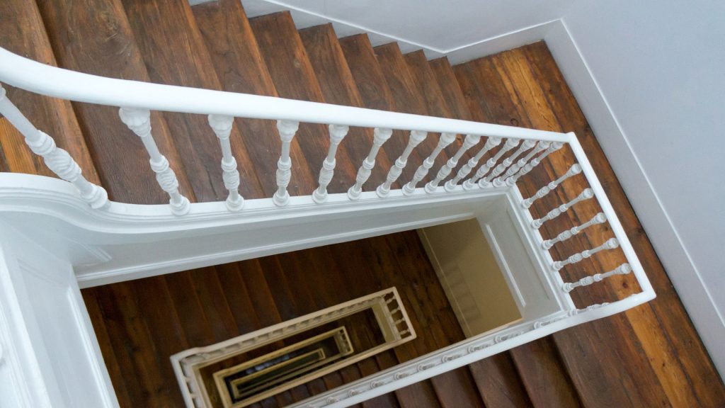 Bild Blogbeitrag Richtergebäudemanagement in Pulheim Thema Treppenhausreinigung Treppenhaus mit weißem Geländer und braunen Holzstufen